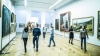 people walking through a museum looking at paintings 